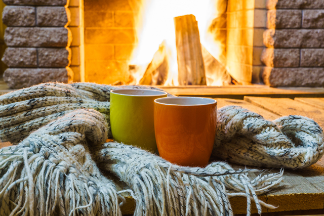 Two mugs for tea or coffee woolen things near cozy fireplace in country house winter vacation horizontal.