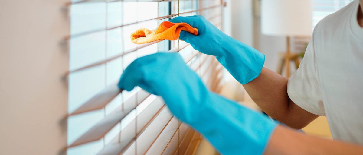 Person dusting blinds with microfiber cloth wearing blue gloves